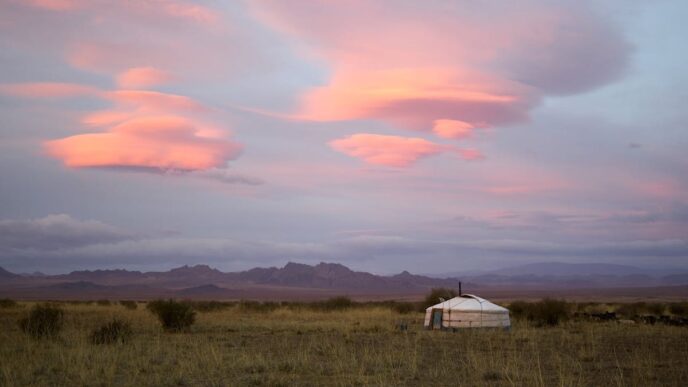 A yurt is seen in the distance in a field, with an evening sky above.