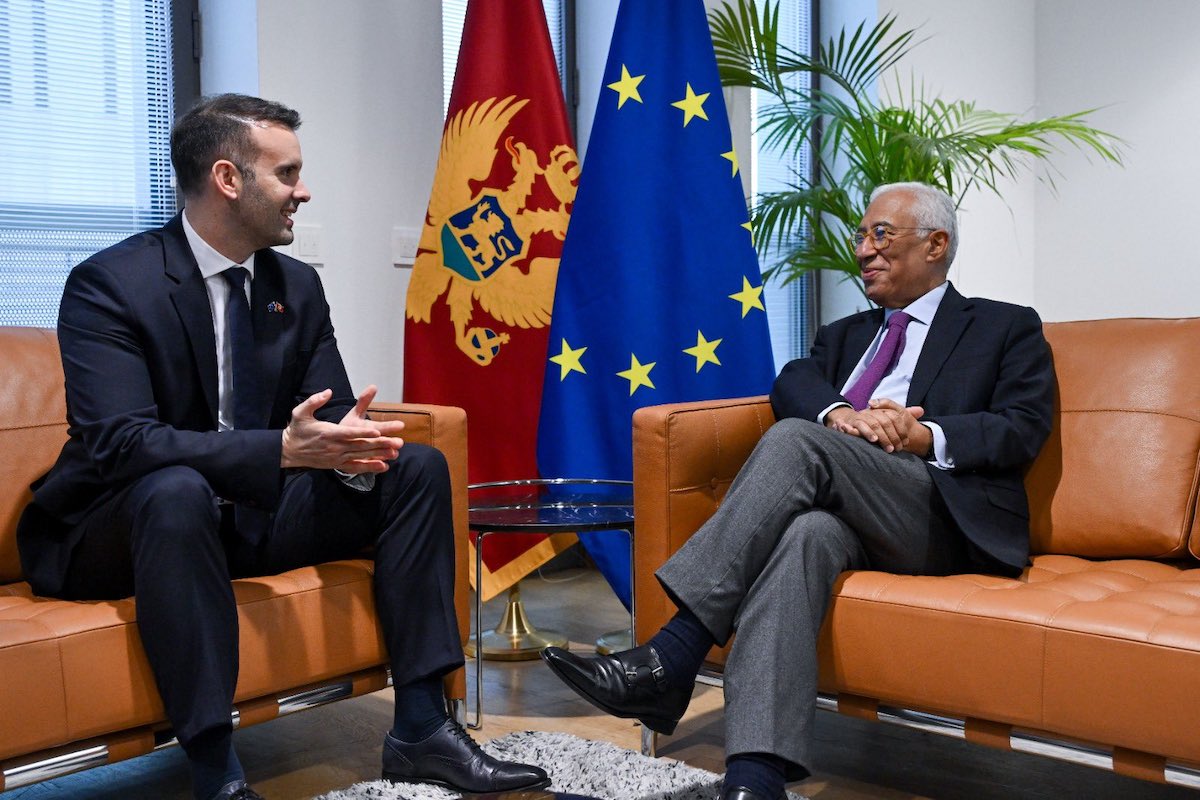 Politicians Antonio Costa sits with Mickey Spajic with flags in the nackground