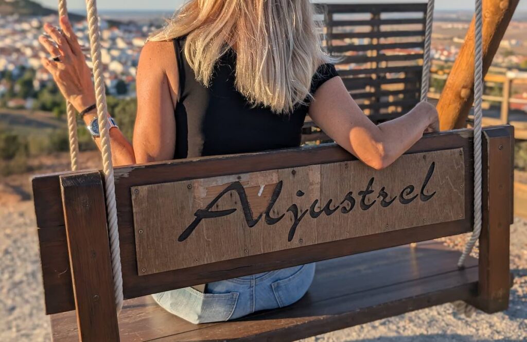 A woman sits on a swing with the name of the town of Aljustrel engraved on it