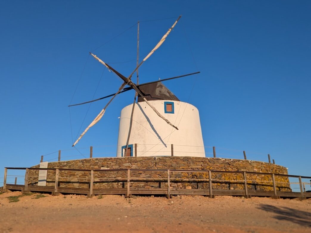 An old fashioned windmill is seen on a hill against a blue sky