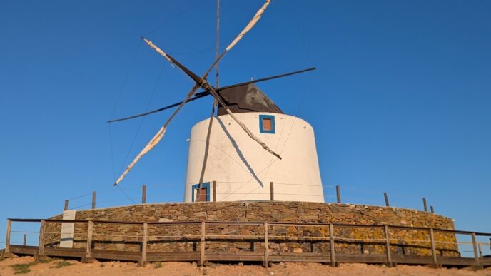 An old fashioned windmill is seen on a hill against a blue sky