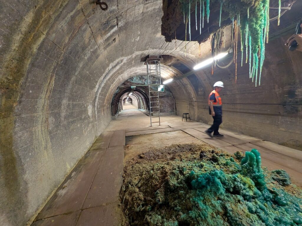 A mining tunnel stretches in to the distance as a worker inspects a wall