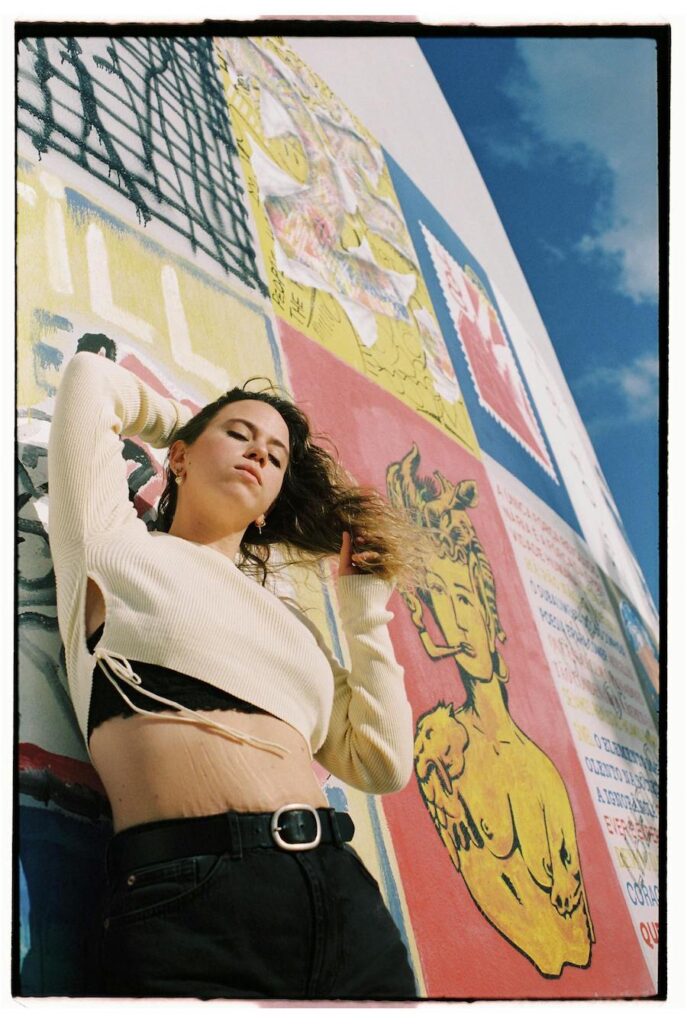 A woman poses in front of graffiti in Lisbon wearing fashionable clothing for a photoshoot