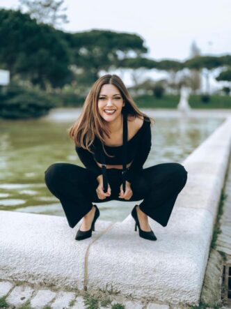 A woman poses outdoors in Lisbon, on a stone wall in fashionable clothing