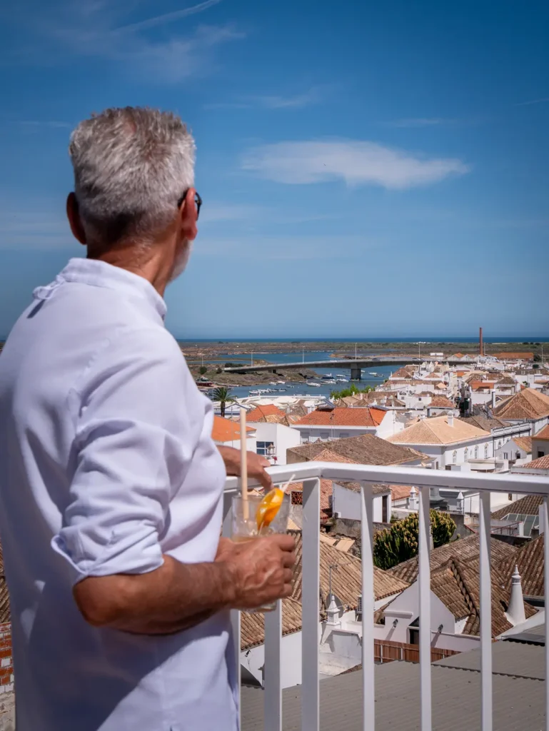 A chef looks over teh city of Tavira while holding a glass