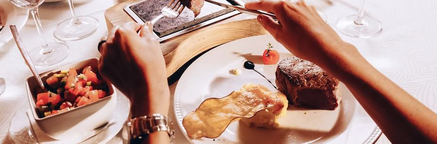 A table is laid with food at a restaurant while a person's hands are poised ready to use a knife and fork