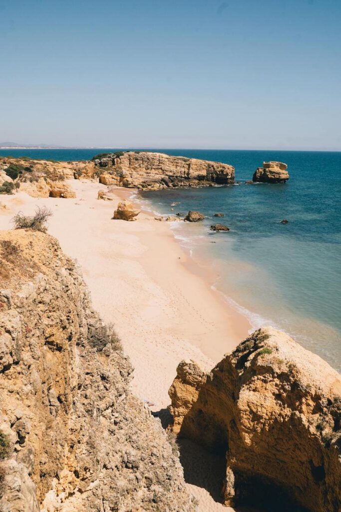 A beach in the Faro District, Portugal, with rocks, sea and a blue sky.