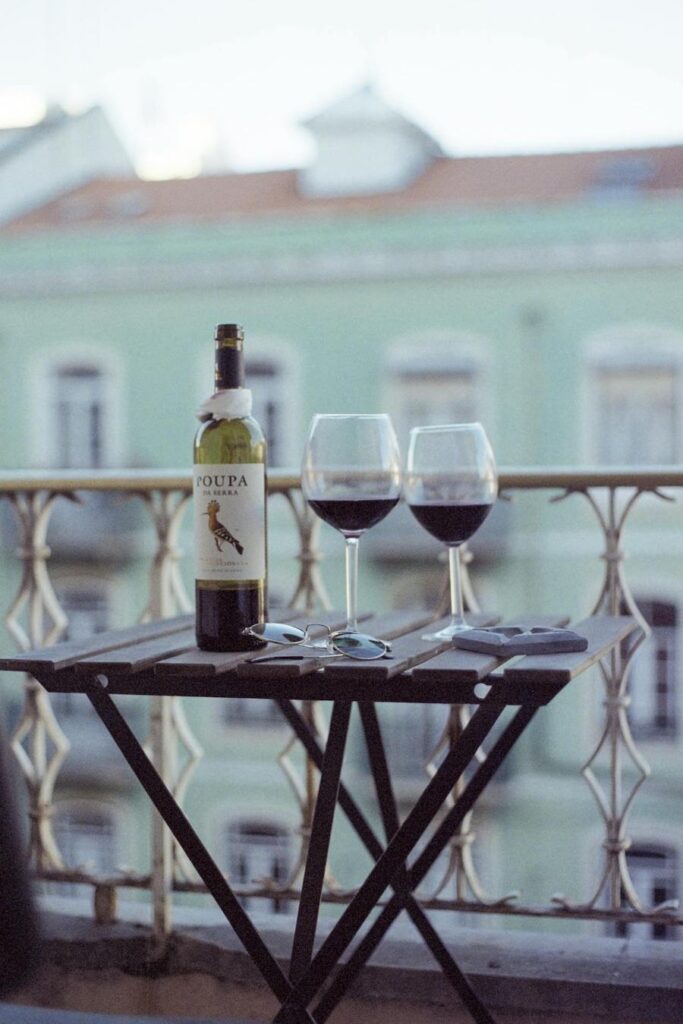 A wine bottle and two glasses on a balcony table overlooking a street in Lisbon