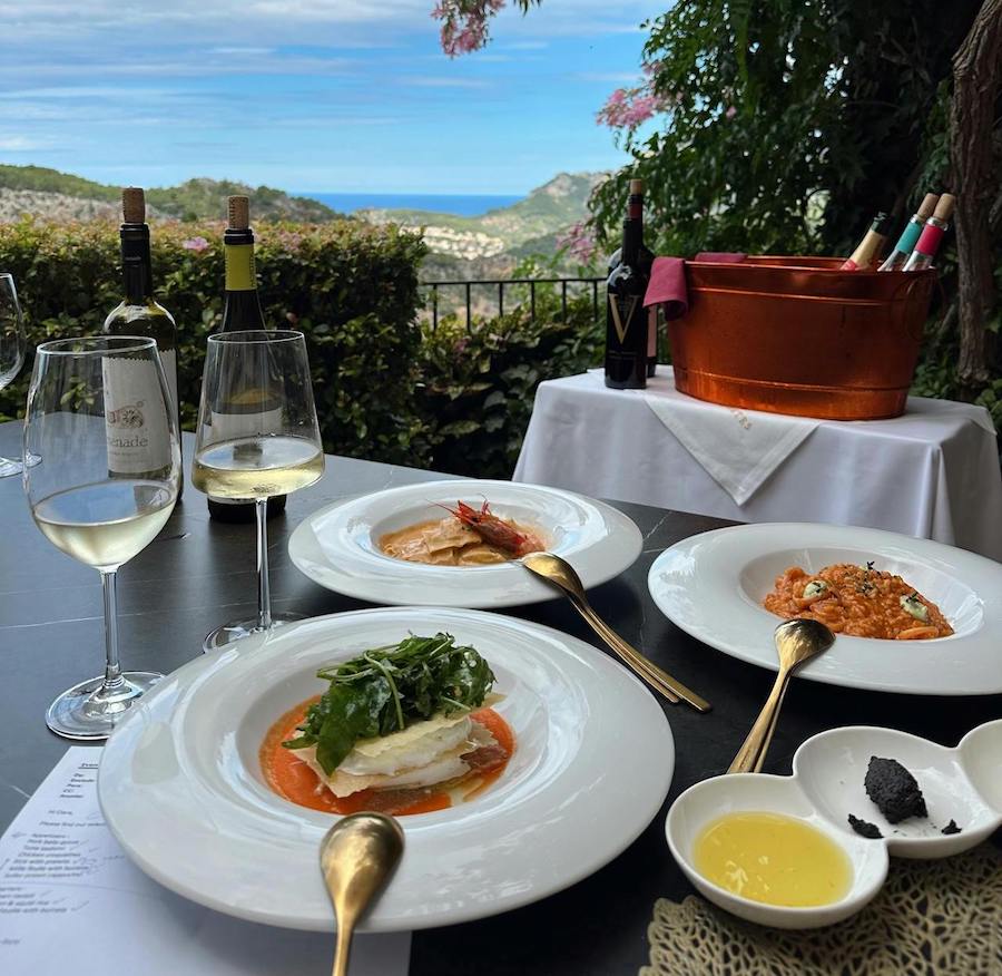 Plates of food ona table outdoors with wine glasses on a table with mountains in the distance