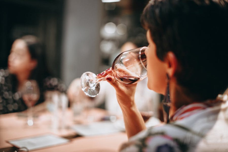 A woman taste wine from a glass sitting in front of a table