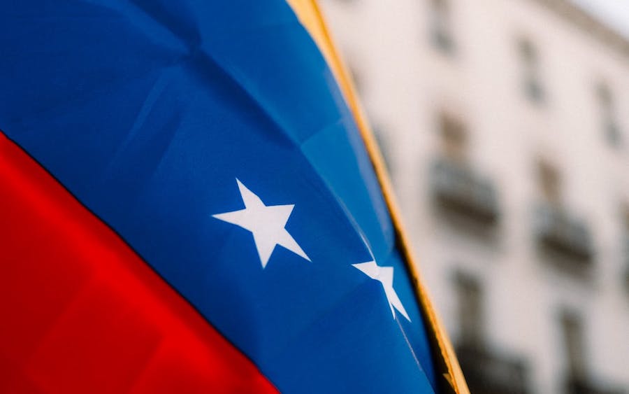 The flag of Venezuela on blows in the wind, with a building out of focus behind